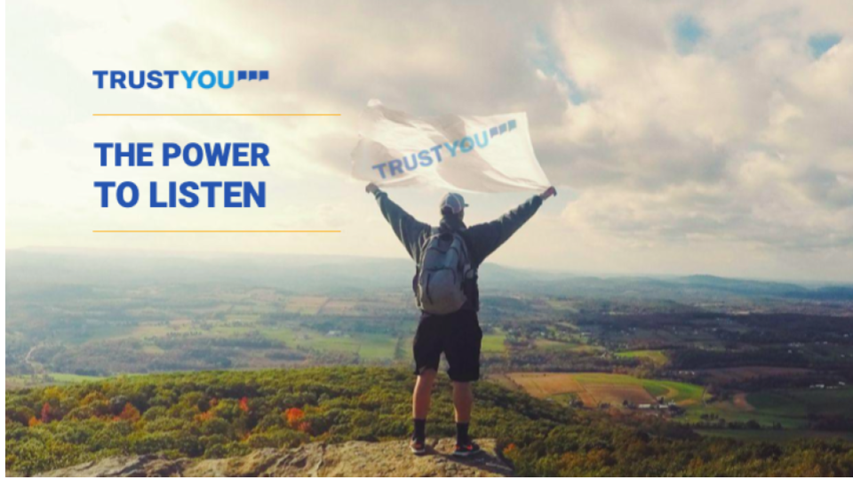 A picture with a man holding a flag that has the TrudtYou logo. The picture includes also the slogan of TrustYou - The Power to Listen.