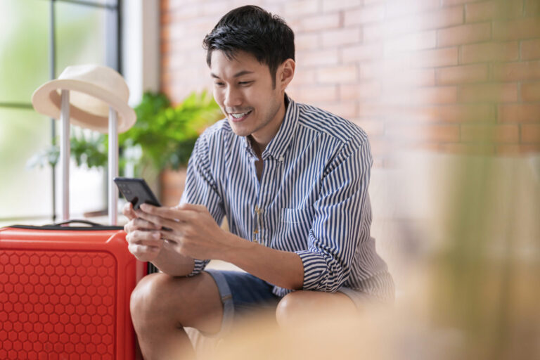 Ready To Travel Abroad,asia Adult Male Man Casual Cloth Sit On Sofa Couch Next To Luggage Travel Bag, Hand Reserve Booking Hotel Room And Flight Ticket By Online Application Smart Device East Travel
